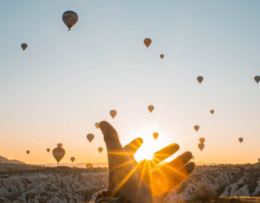 photo of person s hand across flying hot air balloons during golden hour